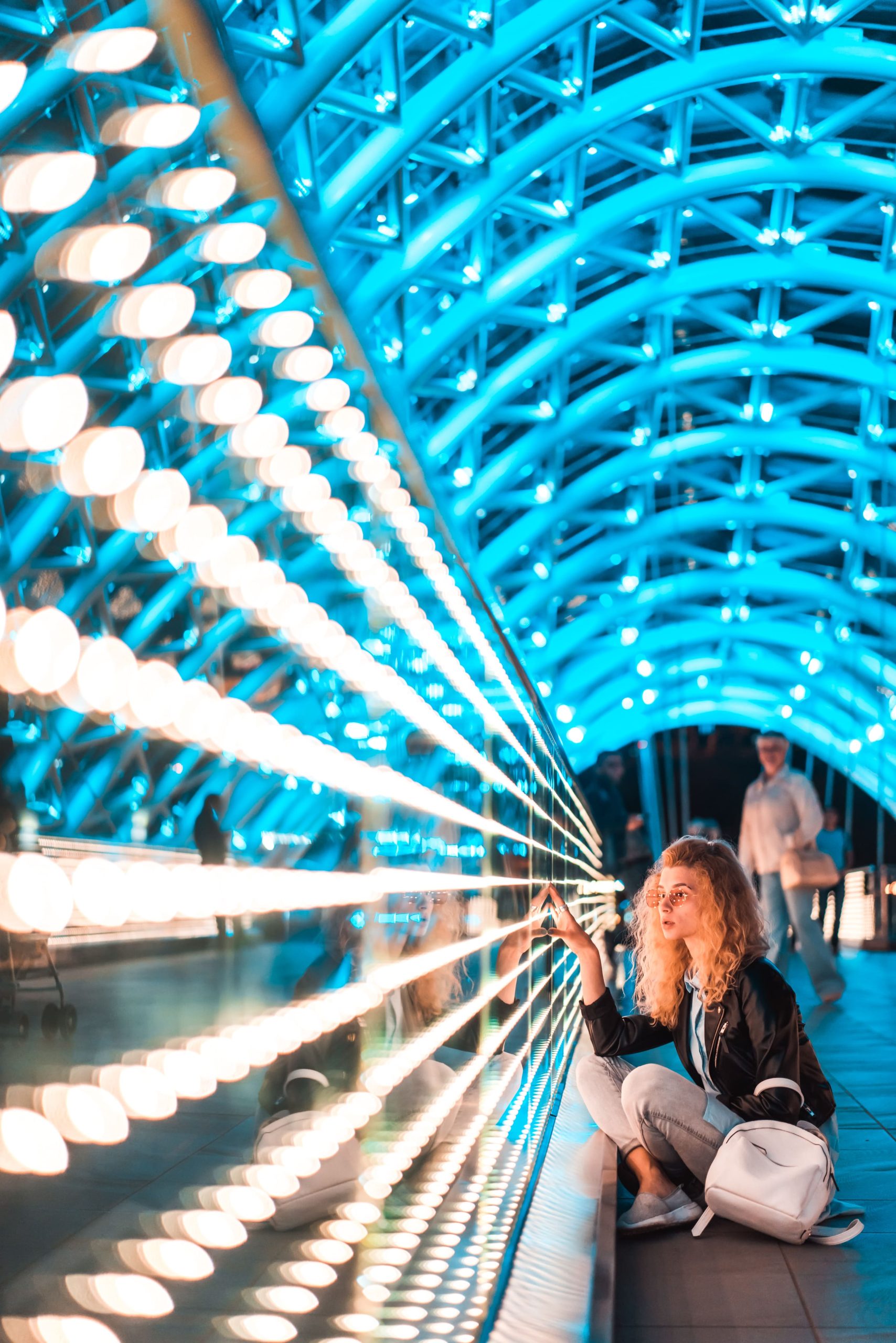 Woman kneeling in a blue-lit future energy design tunnel with modern LED lighting installation